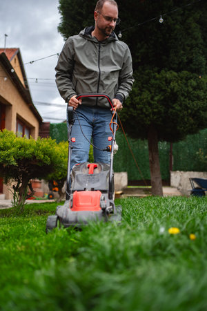 Man mowing a lush green lawn in a cozy backyard on a sunny afternoon, creating a neat and tidy...