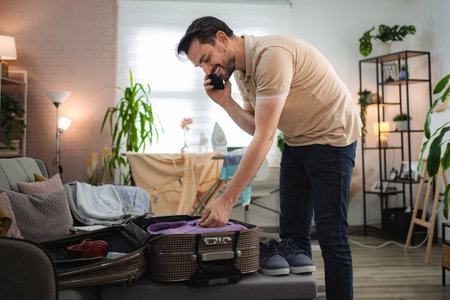 Man talking on the phone while packing suitcase at homeの写真素材