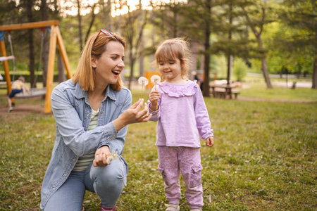 Cheerful daughter and mom blowing dandelions in the park