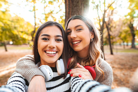 Joyful autumn moments shared by two friends in a sunlit parkの写真素材