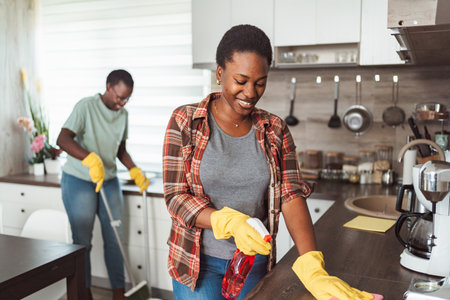 Two African American Women Cleaning the Kitchen Counter and Floor Togetherの写真素材
