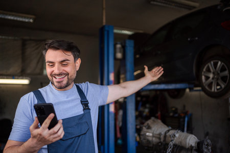 Happy mechanic showing a lifted car while using a smartphone inの写真素材