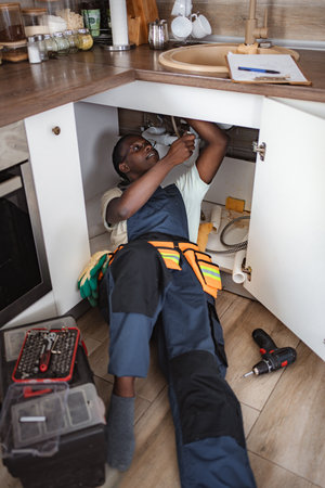 Plumber fixing pipes under kitchen sinkの写真素材