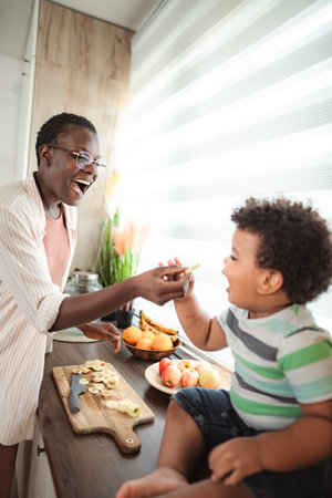 Mother feeding child banana in kitchen for healthy snackの写真素材