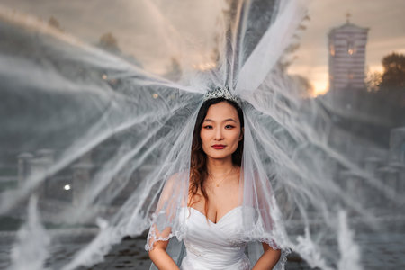 Chinese bride wearing wedding dress and veil by fountainの写真素材