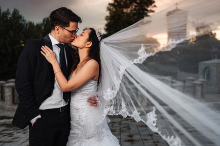 Interracial wedding couple kissing outdoors with flowing veilの写真素材