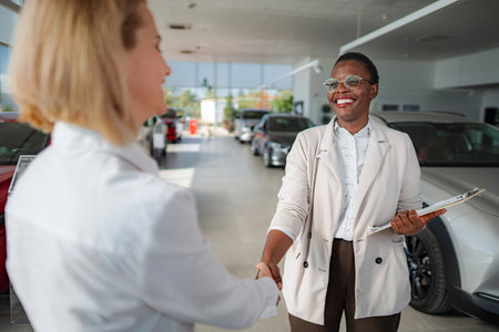 Woman car salesperson shaking hands with customer in showroomの写真素材