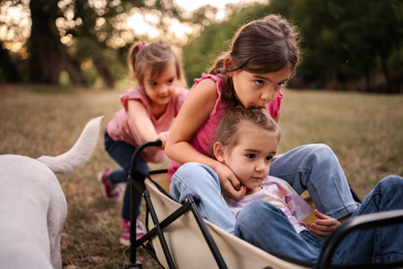 Sisters pushing and kissing little girl in cart in the parkの写真素材