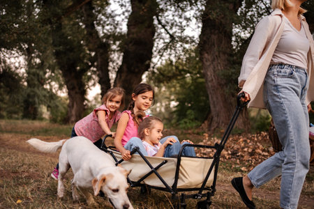 Mother pulling daughters and dog in cart through woods during family picnicの写真素材