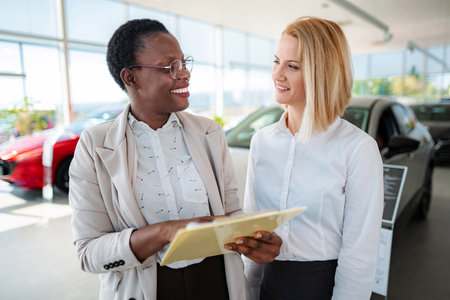 Car saleswoman explaining documents to customer in showroomの写真素材