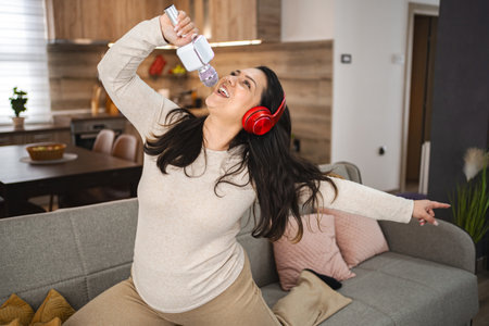 Woman jumping on sofa and singing at homeの写真素材