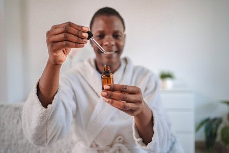 Young woman pouring essential oil from dropper bottle at homeの写真素材
