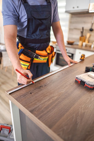 Carpenter measuring wooden kitchen countertop using tape measure and pencilの写真素材