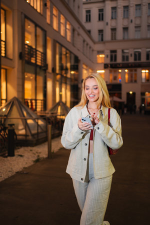 Woman smiling using smartphone walking city street at night in Vの写真素材