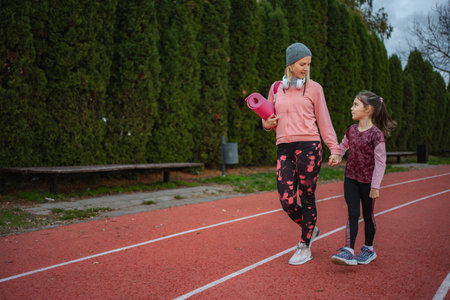 Mother and daughter holding hands walking on running trackの写真素材