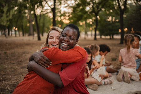 Two cheerful female teachers hugging each other in a parkの写真素材