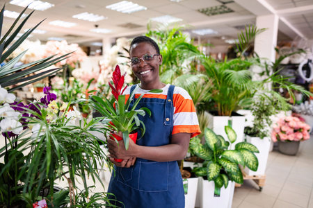Young florist holding a red flower pot, smiling at the camera in a flower shopの写真素材
