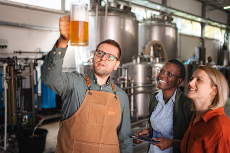 Brewer inspecting craft beer with diverse women in modern breweryの写真素材