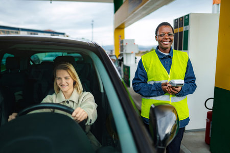 Gas station attendant holding payment terminal interacting with customerの写真素材