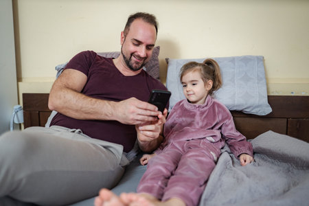 Father and daughter watching smartphone together in bed