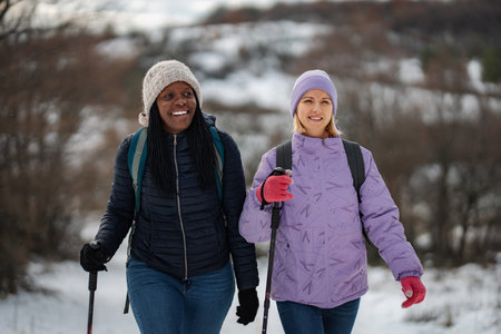 Women friends hiking and walking with poles in winter forestの写真素材