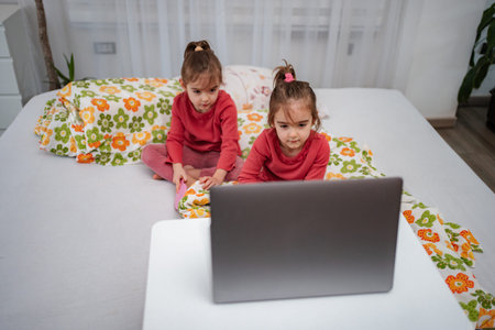 Little twin girls watching laptop on bed at home