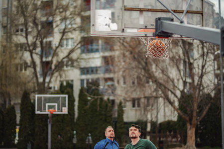 Men watching basketball going through hoop on court
