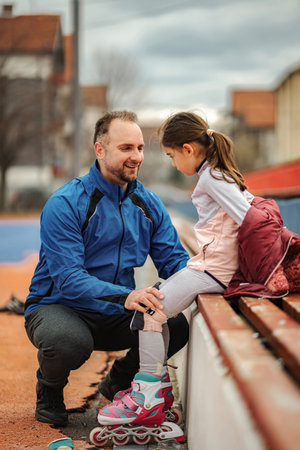 Father teaching daughter how to rollerblade outdoors bonding