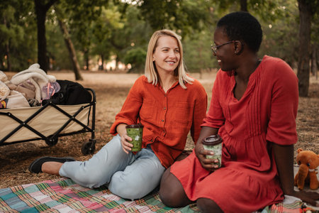 Two friends enjoying a picnic in the park, drinking and chatting