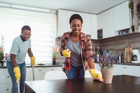 Two cheerful black women cleaning the kitchen table and floor