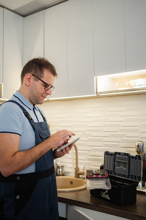 Handyman using tablet near toolbox in modern kitchen