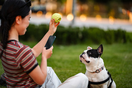 Japanese woman playing with french bulldog, using smartphone