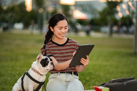 Japanese woman relaxing with French bulldog checking tablet
