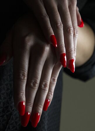 stylishly folded female hands with red manicure on a black backgroundの写真素材