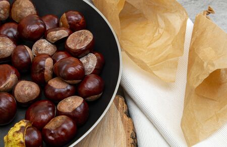 fresh clean shiny chestnuts in a pan with autumn foliage and paper