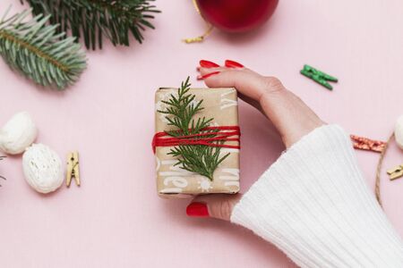 hand made, female hands with beautiful red manicure demonstrate a wrapped gift on pink background