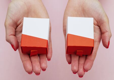 in two female palms are two identical gift boxes on pink background