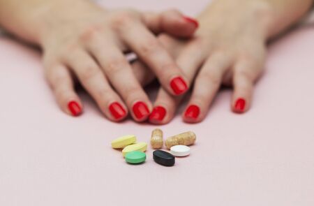pills on the table, girl folded her arms near the tablets, folded hands, on pink background