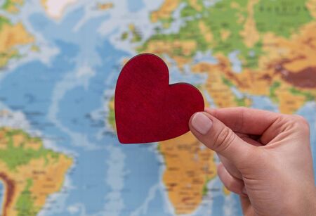 man holds red heart on world map background