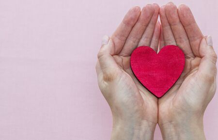 man holds a red heart in his palms on a pink backgroundの写真素材