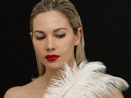 beautiful girl posing with a large white feather on a dark backgroundの写真素材