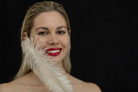 beautiful girl posing with a large white feather on a dark backgroundの写真素材