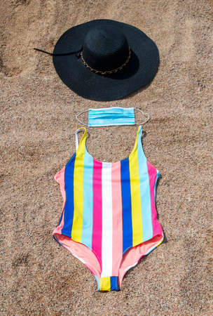 a medical mask with swimsuit and hat on the sand on the beachの写真素材
