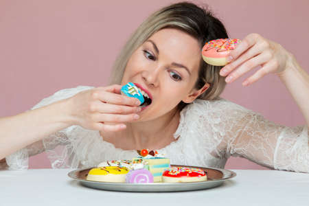 beautiful girl engaging in gluttony of cakes with a tray on a pink backgroundの写真素材