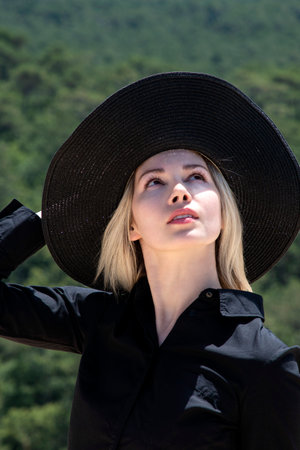 a girl on a sand dune in a black hat and a beautiful forest view