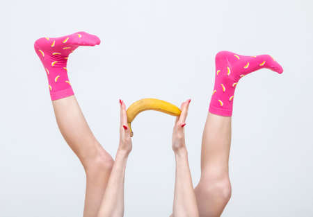 female legs in colorful socks holding banana juggling feet isolated on white backgroundの写真素材