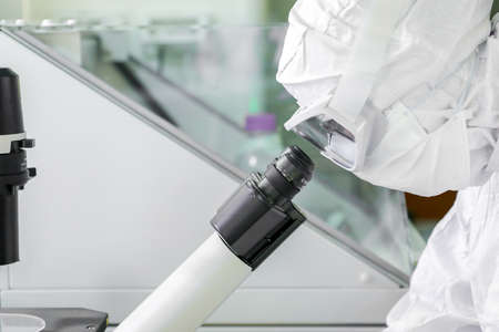 Lab scientists wear protective clothing looking for microscopes while doing medical research in a...