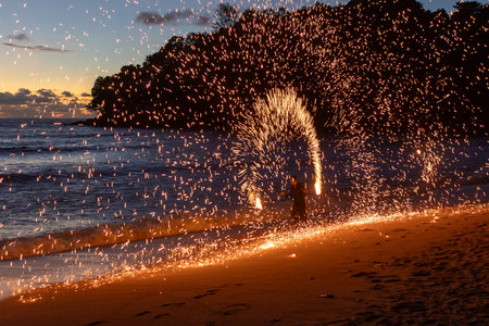 Fire performer lights up the beach, creating beautiful patterns against a sunset backdrop.の写真素材