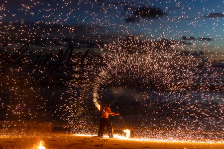 Fire performer lights up the beach, creating beautiful patterns against a sunset backdrop.の写真素材