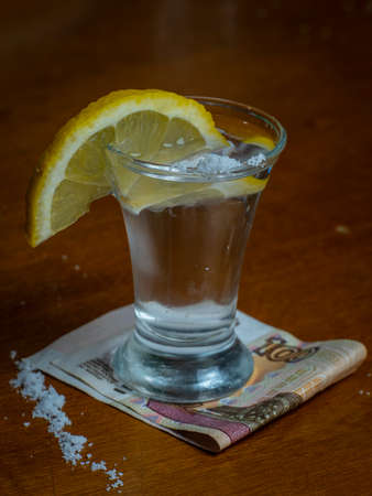 a glass of tequila on the table with lemon and a hundred-ruble billの写真素材